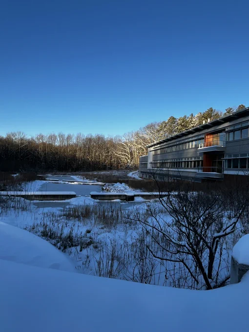A two-story laboratory building overlooks a snow-covered wetland with terraced pools.