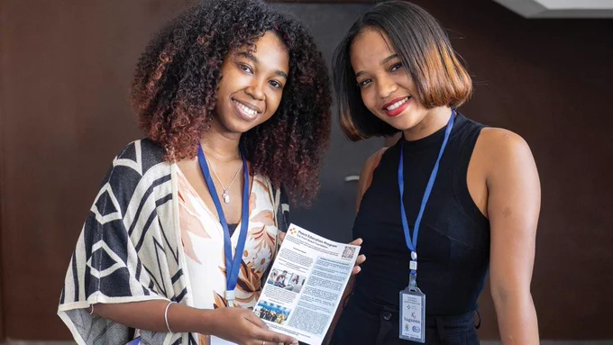 Two smiling young women hold up a brochure about The Prem Rawat Foundation's Peace Education Program