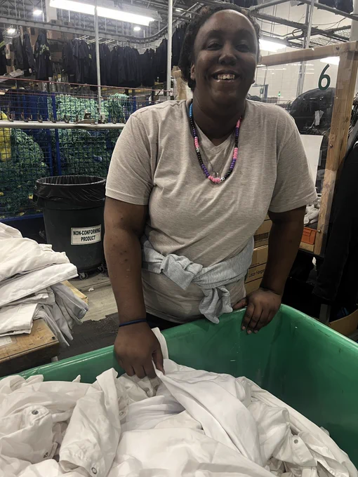 A woman smiles while sorting white uniforms from a green bin inside a UniFirst facility.