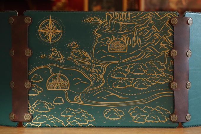 A close up of a dark green leather DM screen panel standing upright on a table, flanked by two brown connectors. The panel depicts a fantasy map.