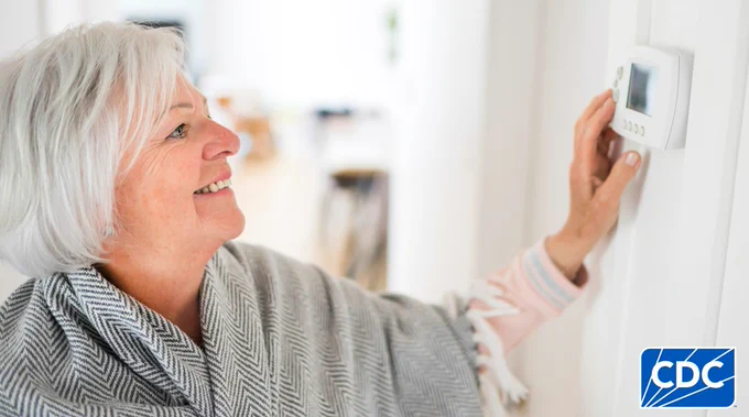 Person adjusting a thermostat on a wall.