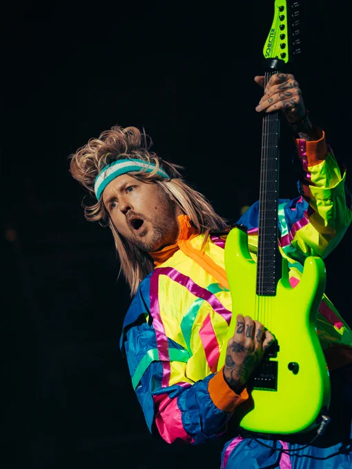 Ein Musiker in bunter Kleidung spielt leidenschaftlich eine E-Gitarre auf der Bühne.