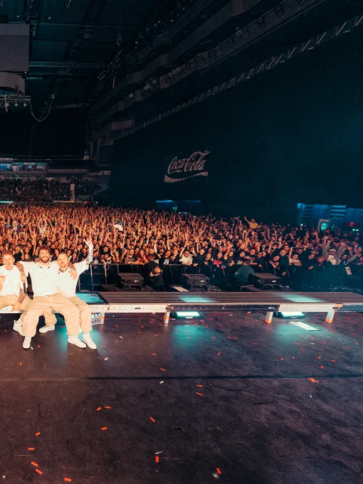 Eine große Menge enthusiastischer Menschen bei einer live Musikaufführung, die eine große Leinwand mit dem Coca-Cola-Logo im Hintergrund zeigt.