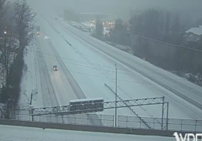 Snow-covered I-66 near Fair Oaks with sparse traffic and light snowfall reducing visibility in a winter landscape.