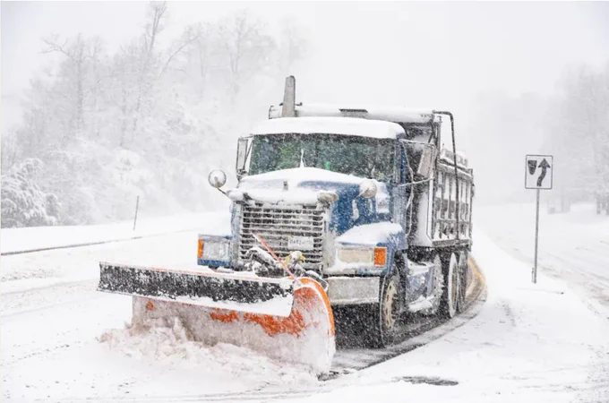 Blue snowplow truck clearing heavy snow from a road during a winter storm.