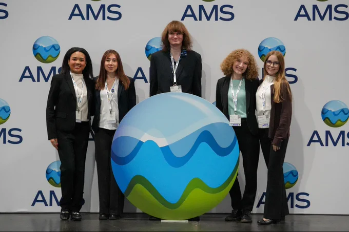 A group of student attendees in front of the AMS backdrop.
