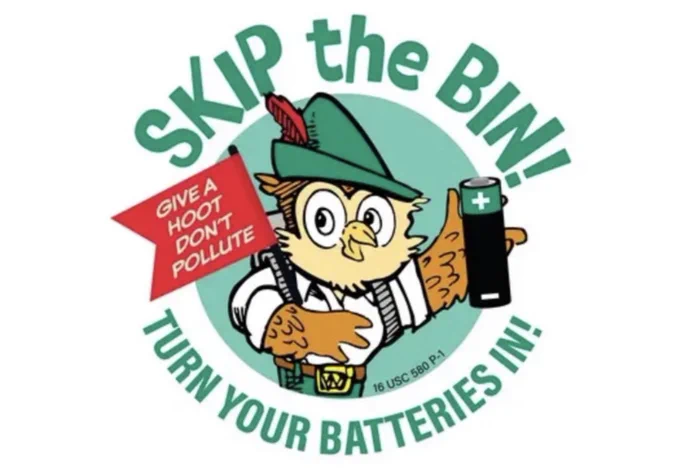 A circular public service graphic featuring Woodsy Owl wearing a green ranger hat with a feather. He is holding a red flag that reads “Give a hoot, don’t pollute” and a battery with a plus sign. Green text around the circle reads “Skip the bin!” at the top and “Turn your batteries in!” at the bottom, on a white background.
