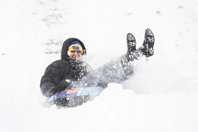 Person sledding down a snowy hill wearing a "Pitt" hat.