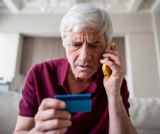 A person using a credit card and making a phone call while looking concerned.
