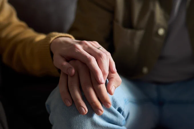 A close up shot of two people holding hands, with one person comforting the other.