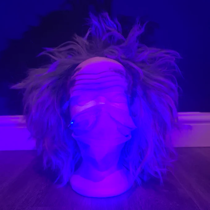 Photograph of a mannequin head wearing a wig and face mask in purple light.