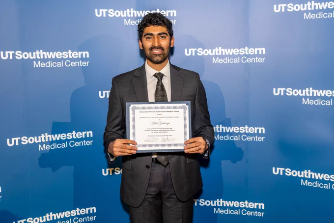 Person holding a diploma in front of a UT Southwestern Medical Center backdrop.
