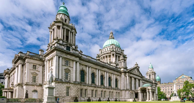 Historic Belfast City Hall with its green domes under a partly cloudy blue sky.
