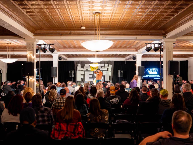 An indoor event at LaughFest with an audience watching a performer on stage under a banner displaying the festival's name.