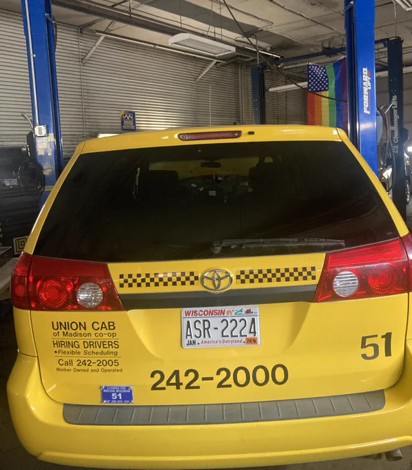 A yellow taxi cab that says union cab cooperative of madison and a rainbow pride flag hangs in the background of the shop. 