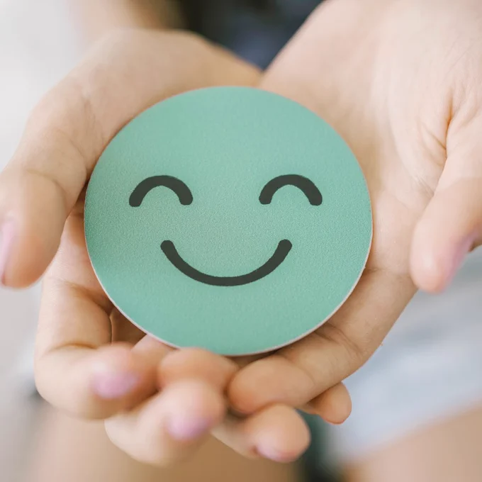 Unknown person holds smiley face on green circle. 
