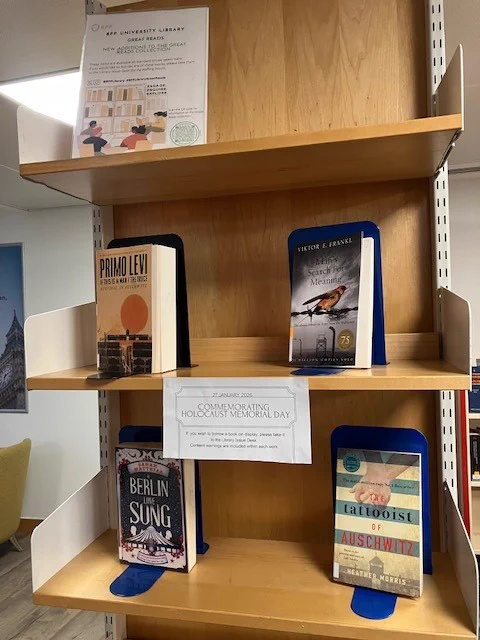 A wooden bay of shelves featuring a a series of books chosen to commemorate Holocaust Memorial Day. From left to right: upper shelf: ‘If This Is A Man/The Truce’ by Primo Levi, ‘Man’s Search for Meaning’ by Viktor E. Frank. Lower shelf: ‘A Berlin Love Song’ by Sarah Matthias, ‘The Tattooist of Auschwitz’ by Heather Morris. 