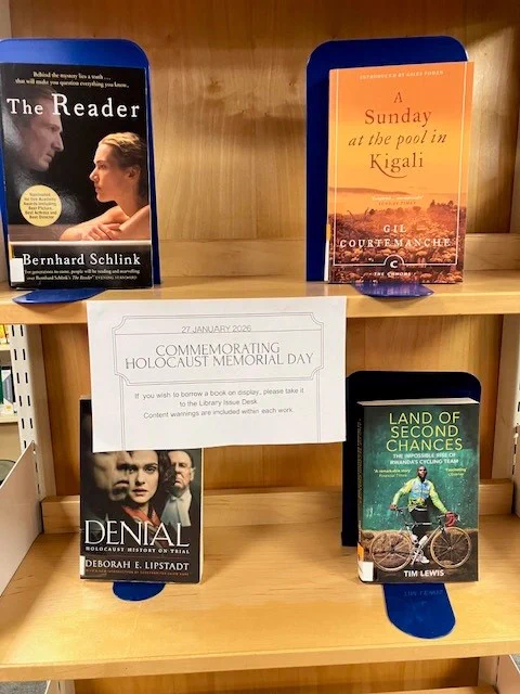 A wooden bay of shelves featuring a a series of books chosen to commemorate Holocaust Memorial Day. From left to right: upper shelf: ‘The Reader’ by Bernhard Schlink, ‘A Sunday at the Pool in Kigali’ by Gil Courtemanche. Lower shelf: ‘Denial: Holocaust History On Trial’ by Deborah E. Lipstadt, ‘Land of Second Chances’ by Tim Lewis.