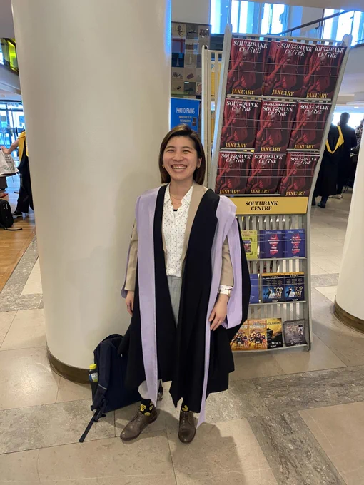A person smiles in lavendar trimmed graduation robes