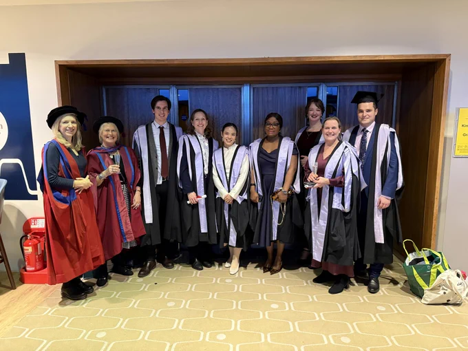Students in their lavender trimmed graduation robes smile with teachers in their red robes.