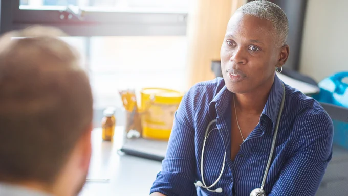 A doctor faces her patient, wearing a stethoscope around her neck, to deliver test results.
