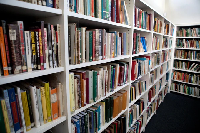 A corner of a room with bookshelves, full of brightly coloured books filling the shelves.