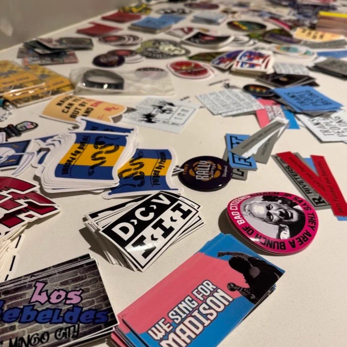 A tabletop covered with various colorful stickers featuring slogans, logos, and graphic designs spread out randomly.
