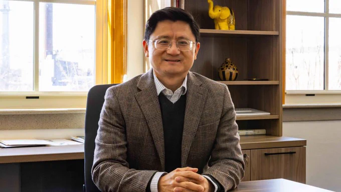 A man named Kui Xie sits at a desk in his office.