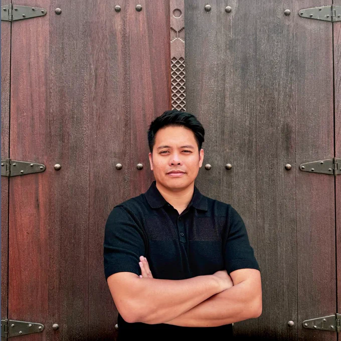 Alfredo Marco Pradil of Hanken Design Co. stands in front of a large wooden door with decorative metal accents.