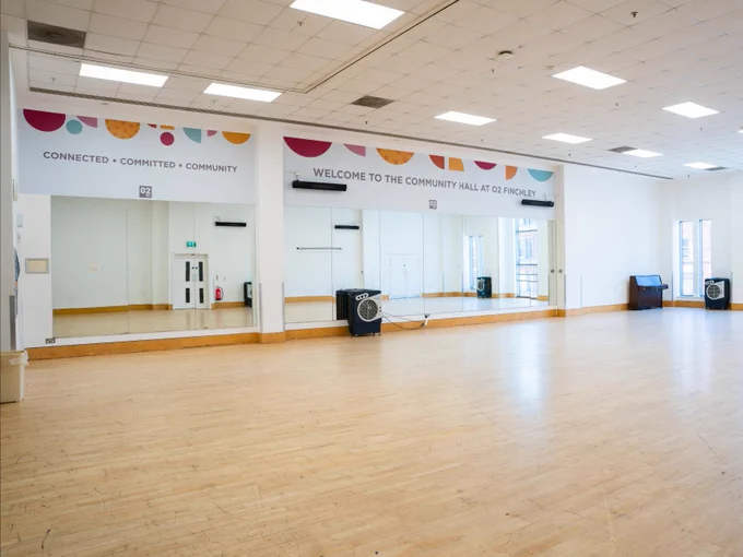 Interior view of the Community Hall at Finchley featuring a spacious room with a wooden floor, along with colourful banners on the walls promoting connectivity, commitment, and community.