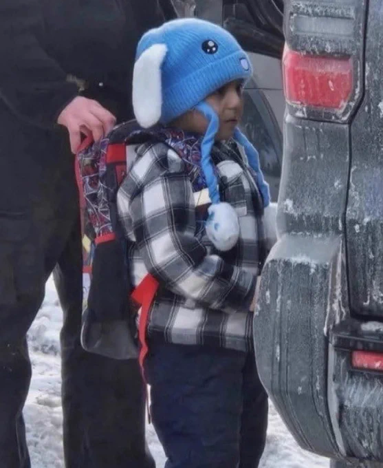 Photo of Liam Ramos In a blue hat and plaid shirt and backpack being put in a dark car