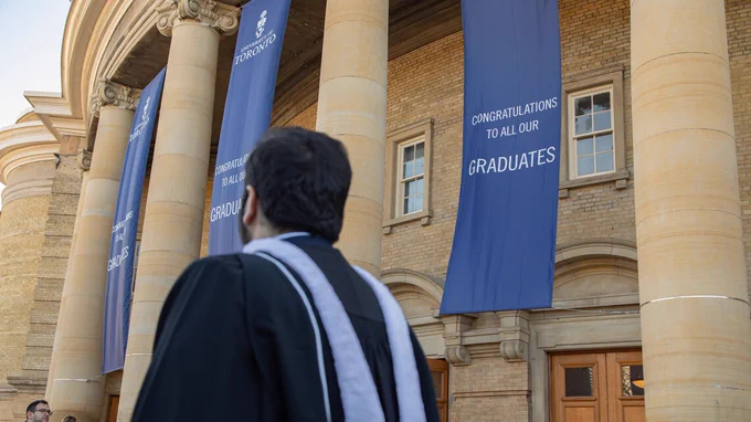 A graduating student walks past a banner that reads, "Congratulations to all our graduates."

