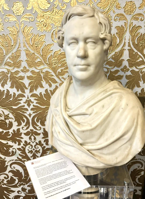 Photo of a bust with gold patterned wallpaper behind.