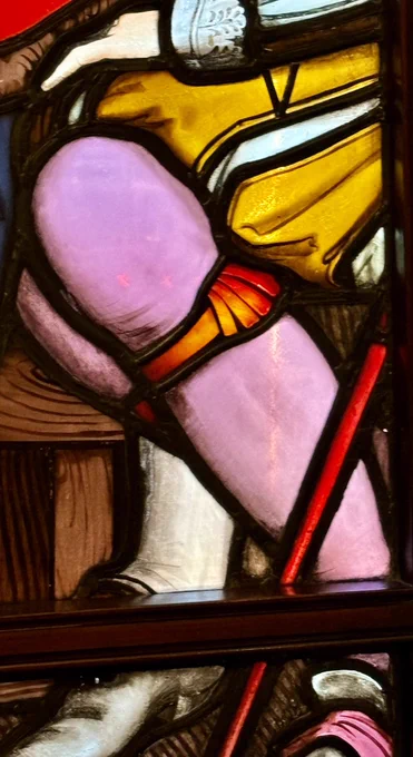 Close up photo of a stained glass window showing a man’s bright pink hose.