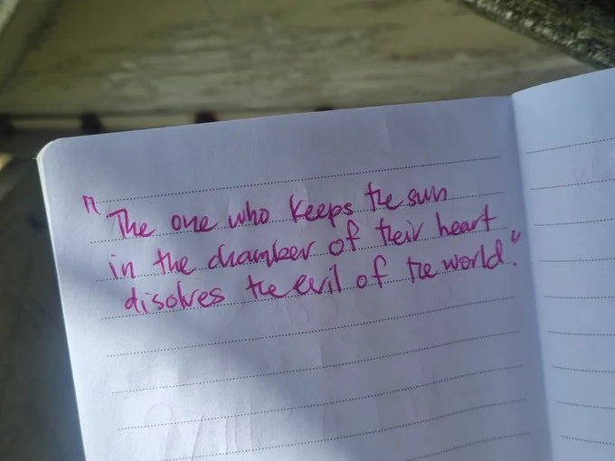 This photo depicts a close-up of a small notebook where someone has written the following in bright pink ink: the one who keeps the sun in the chamber of their heart dissolves the evil of the world. 