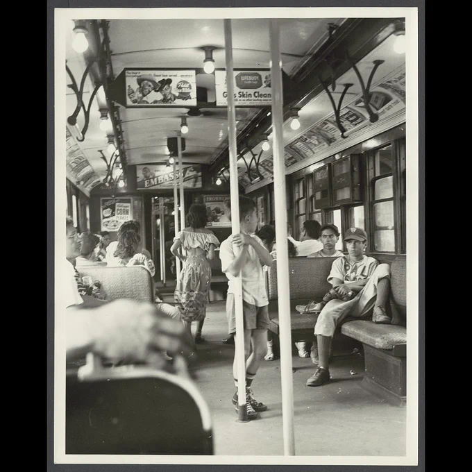 A variety of subway passengers sitting and standing on a car.