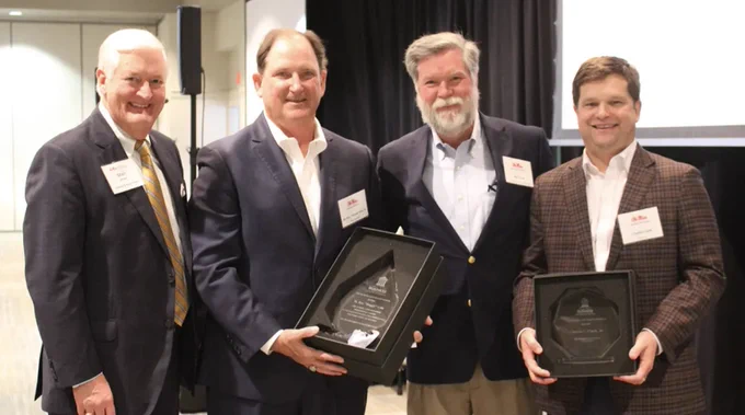 Four individuals posing with awards at an event, with two holding plaques.