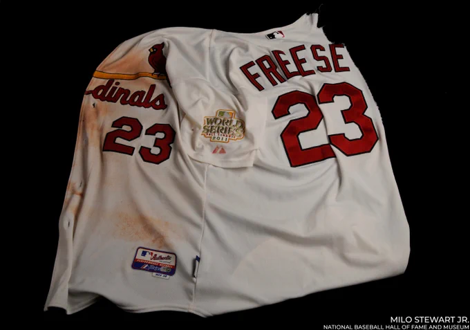 David Freese's torn white number 23 Cardinals uniform with right side front missing. There are button holes with "dinals" / "23" on the front, and the left sleeve has a 2011 World Series patch. (Milo Stewart Jr./National Baseball Hall of Fame and Museum)
