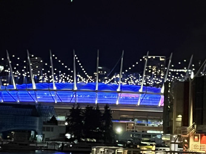 Football stadium with spiked suspension ropes lit in white, roof and round walls lit in blue, lights reflecting in foreground