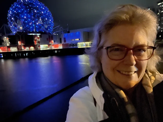 Woman wearing glasses and white jacket in foreground, geodesic dome lit in blue in background
