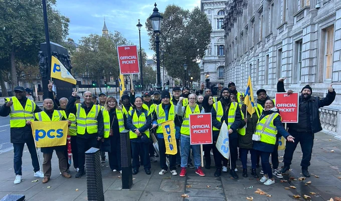 Large group of people in high vis jackets with PCS flags and placards standing in a London street