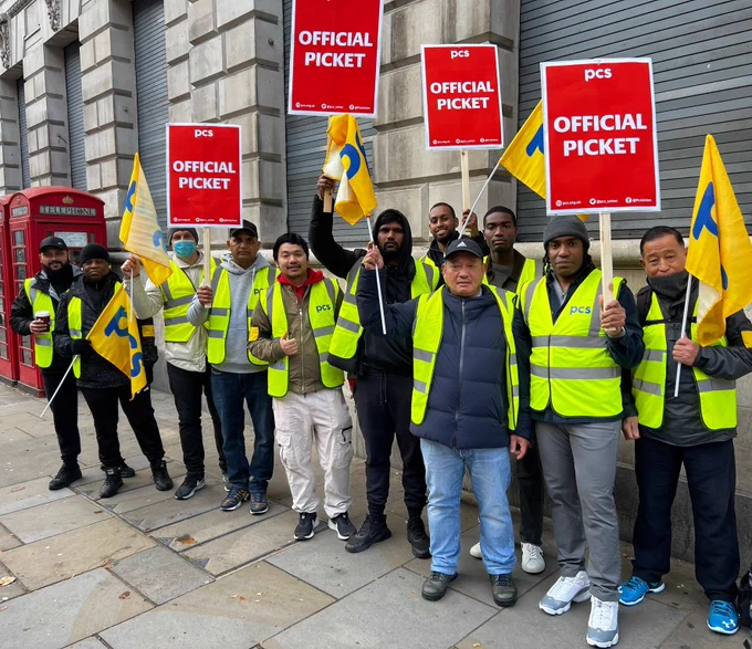 Long line of people in high vis jackets with PCS flags and placards