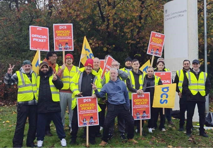 Big group of people in high vis jackets with PCS flags and placards standing in front of autumn trees