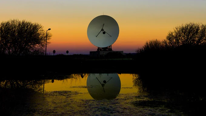 Satellite antenna pointing forwards during sunset, reflected by a lake