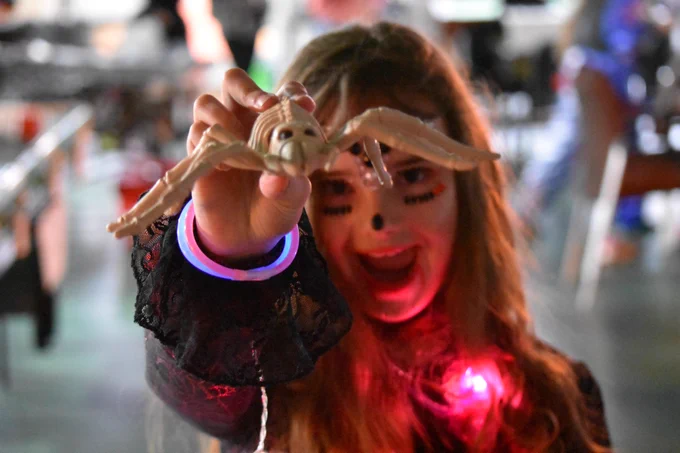 A player in a halloween outfit holding a fake spider to the camera.