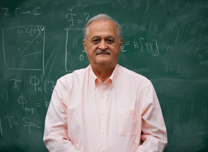 Prof Samson Shatashvili, wearing a pink shirt, standing in front of a blackboard with theorems written on it.