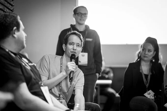 Bernhard Kau sitting between other audience members, holding a microphone to ask a question.