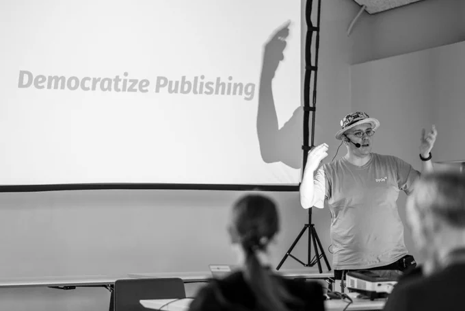 Robert Windish gesticulating dramatically during his talk, in front of a screen that says "Democratize Publishing" 