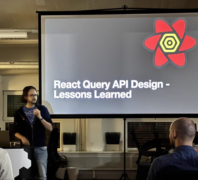 Dominik standing in front of a big projector screen with the text “react query api design - lessons learned”