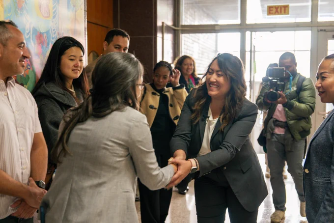 Chancellor Ramos is shaking hands as she is greeted at the front entrance of a middle school.